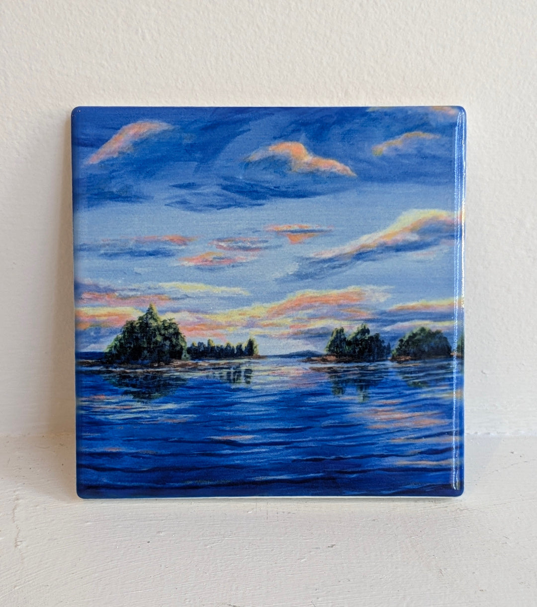 Square ceramic tile with a painting of a lake and sky with  a sunset background