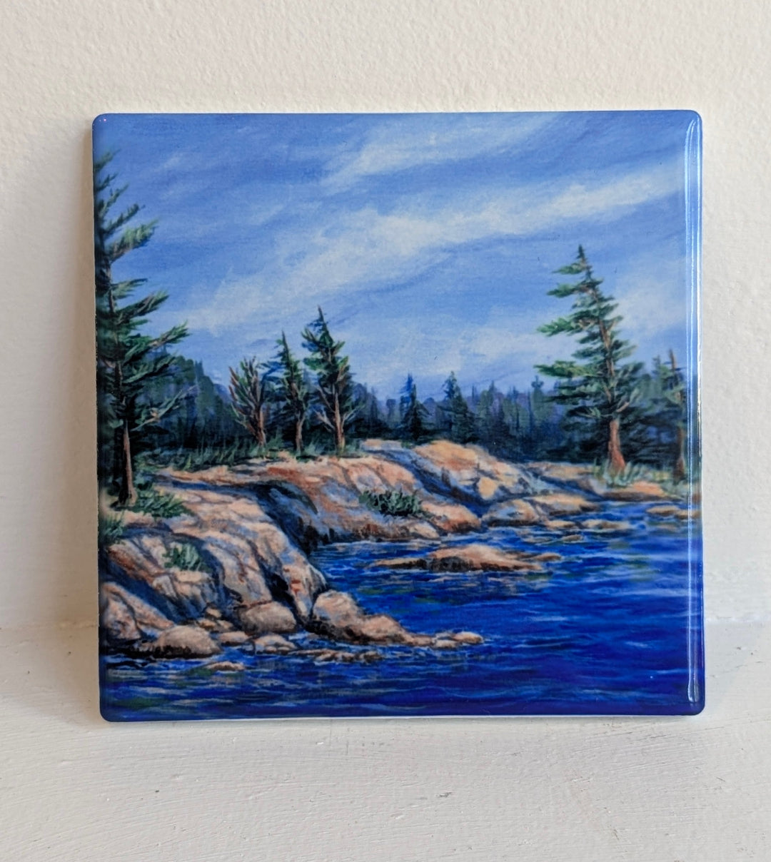 Square painting of a landscape with trees, rocks, and water on a white background
