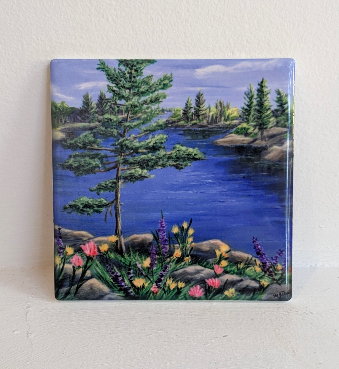 Painting of a serene lakeside scene with trees and flowers on a square tile.
