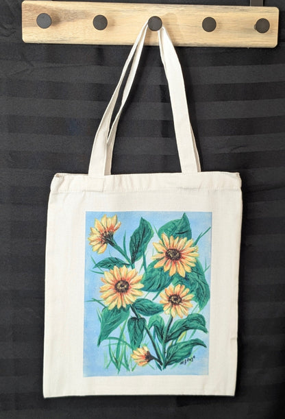 Tote bag with sunflower design hanging on a wooden hook against a black background